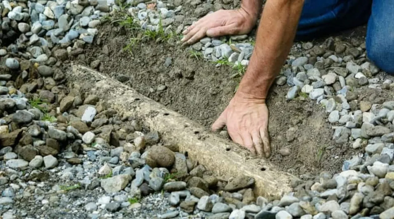 Perforated drain pipe being set into a gravel-filled French drain trench