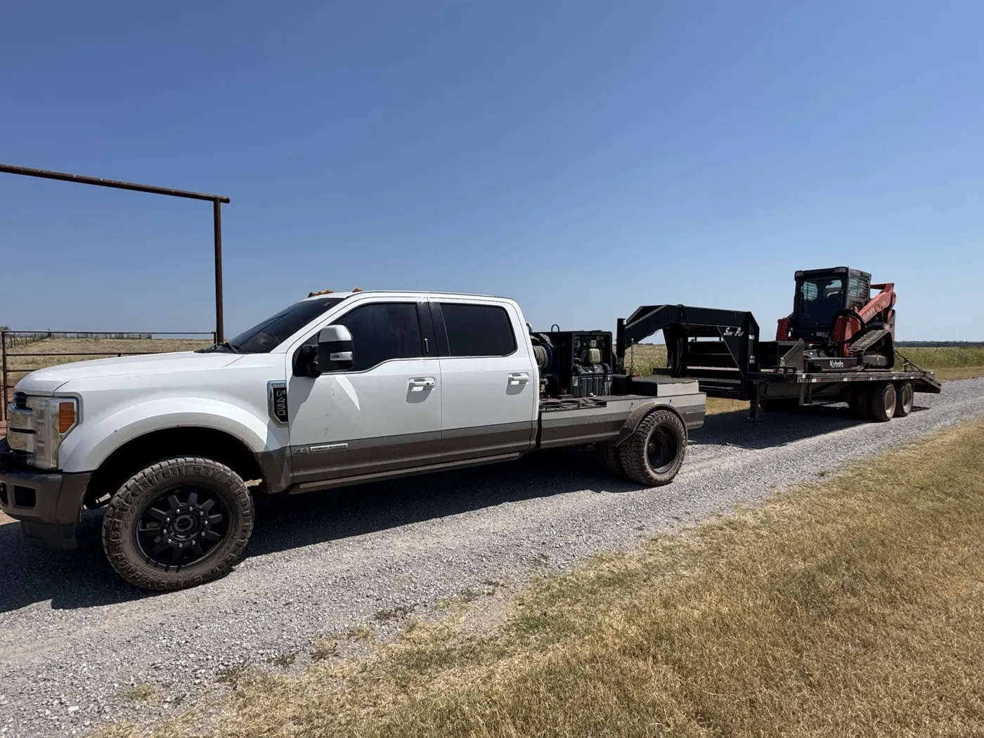 Flatbed truck hauling the track skid steer on a gooseneck trailer, headed to a job